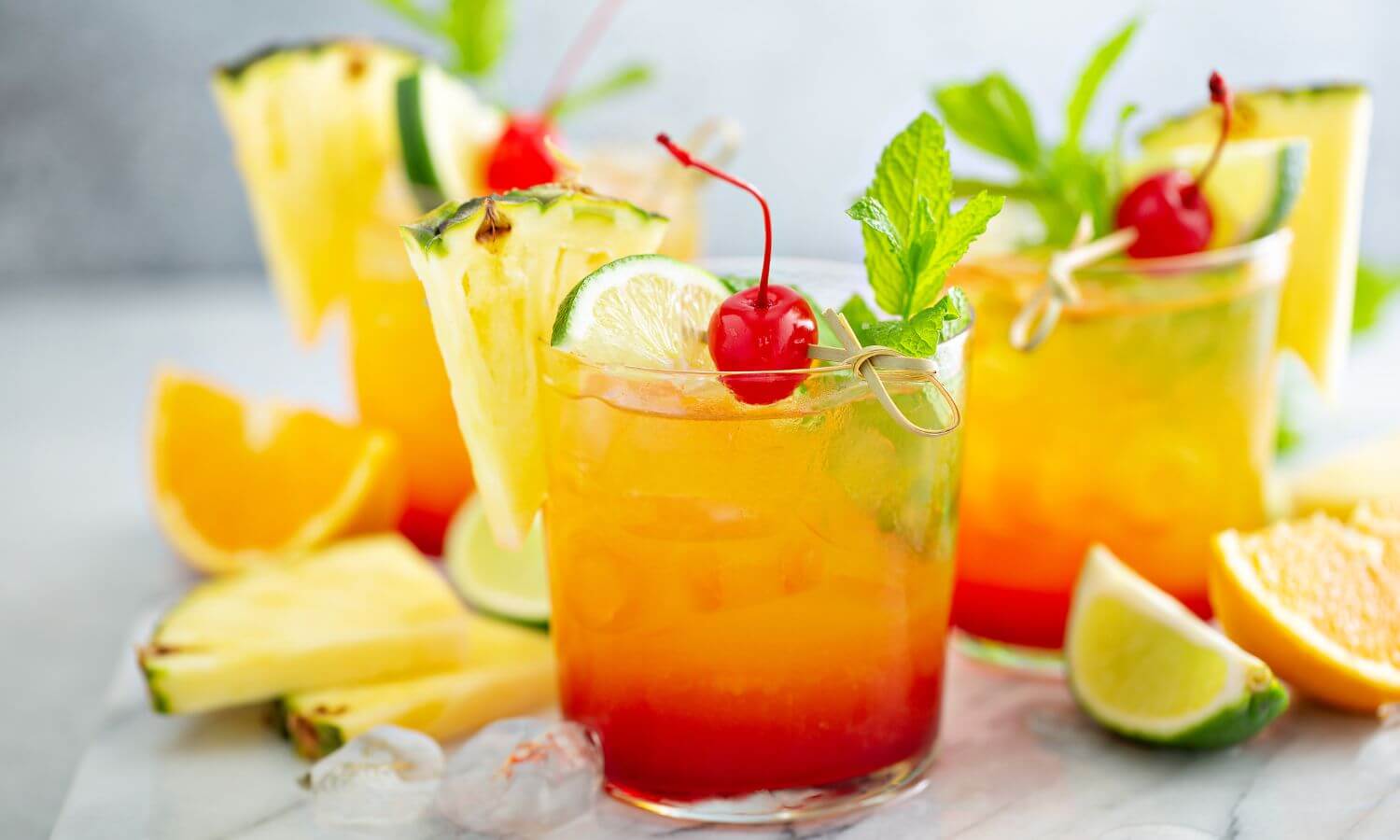Tequila Sunrise, a classic tequila cocktail. These ones are garnished with pineapple, lime mint and a glacier cherry