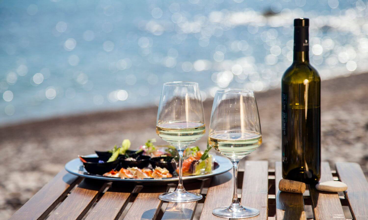 A plate of food and glasses of wine on a table by the ocean at the Festival Gourmet Internacional in Puerto Vallarta