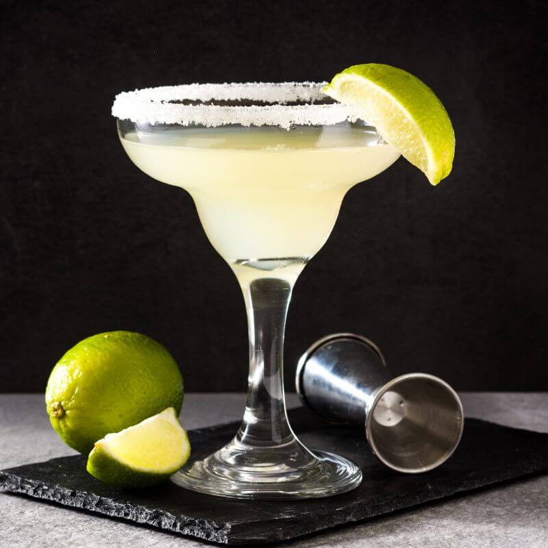 A glass of margarita with salt and lime on the rim, sat on a stone coaster.