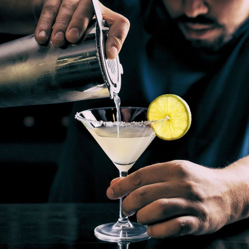 A man pouring a margarita from a shaker into a salt rimmed glass. The History of the Margarita