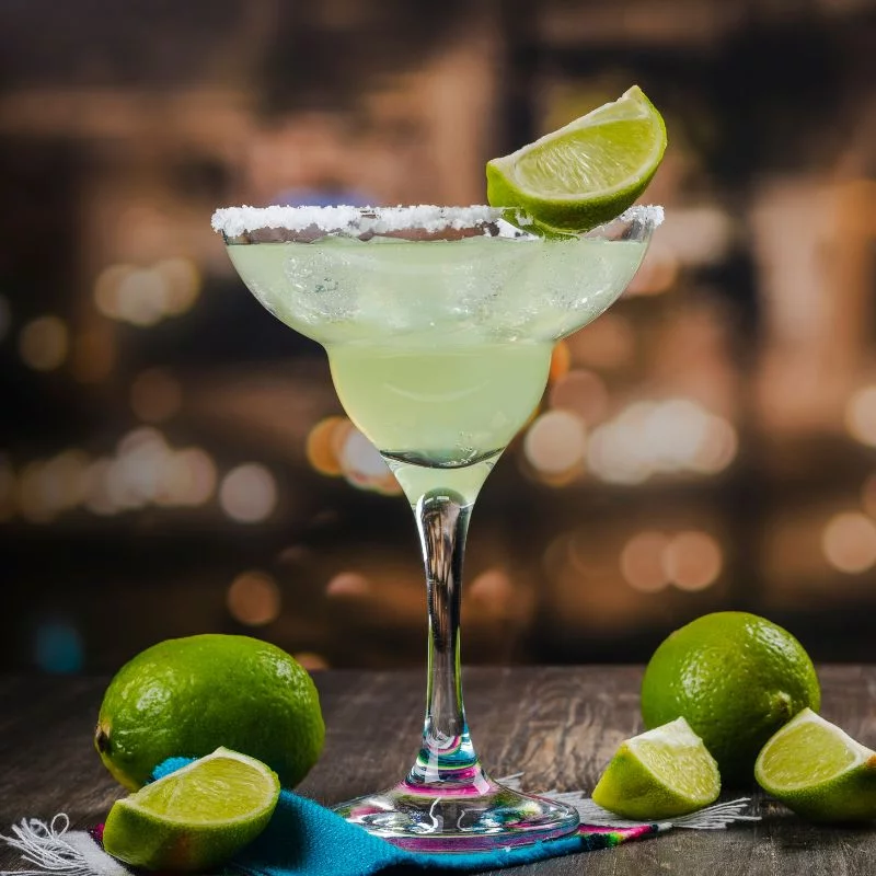 The True History Of The Margarita Cocktail 2 Margarita cocktail on a bar with limes
