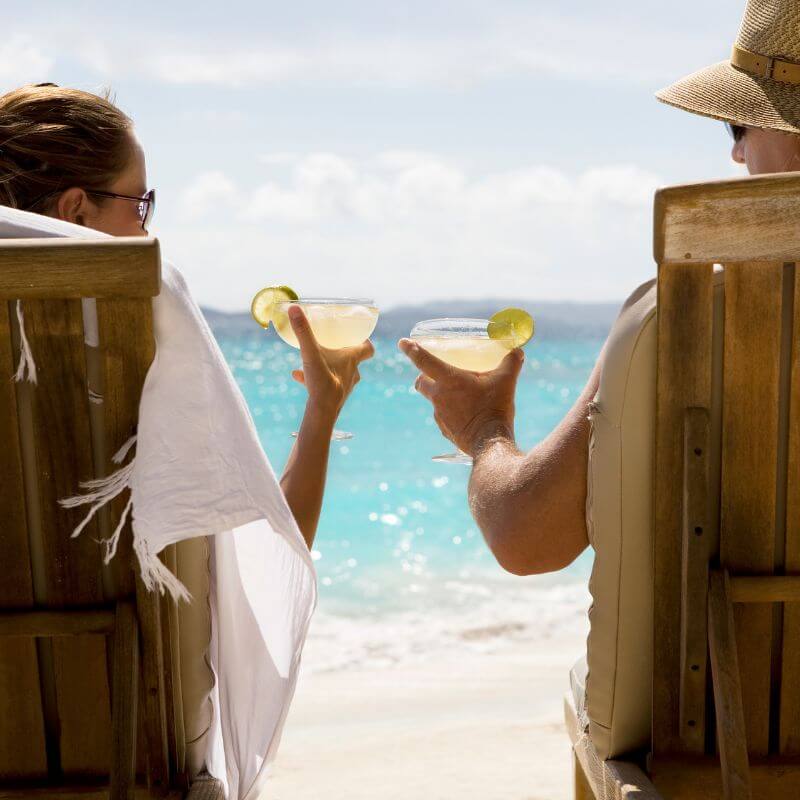 A couple raising margaritas in beach chairs in front of the ocean.