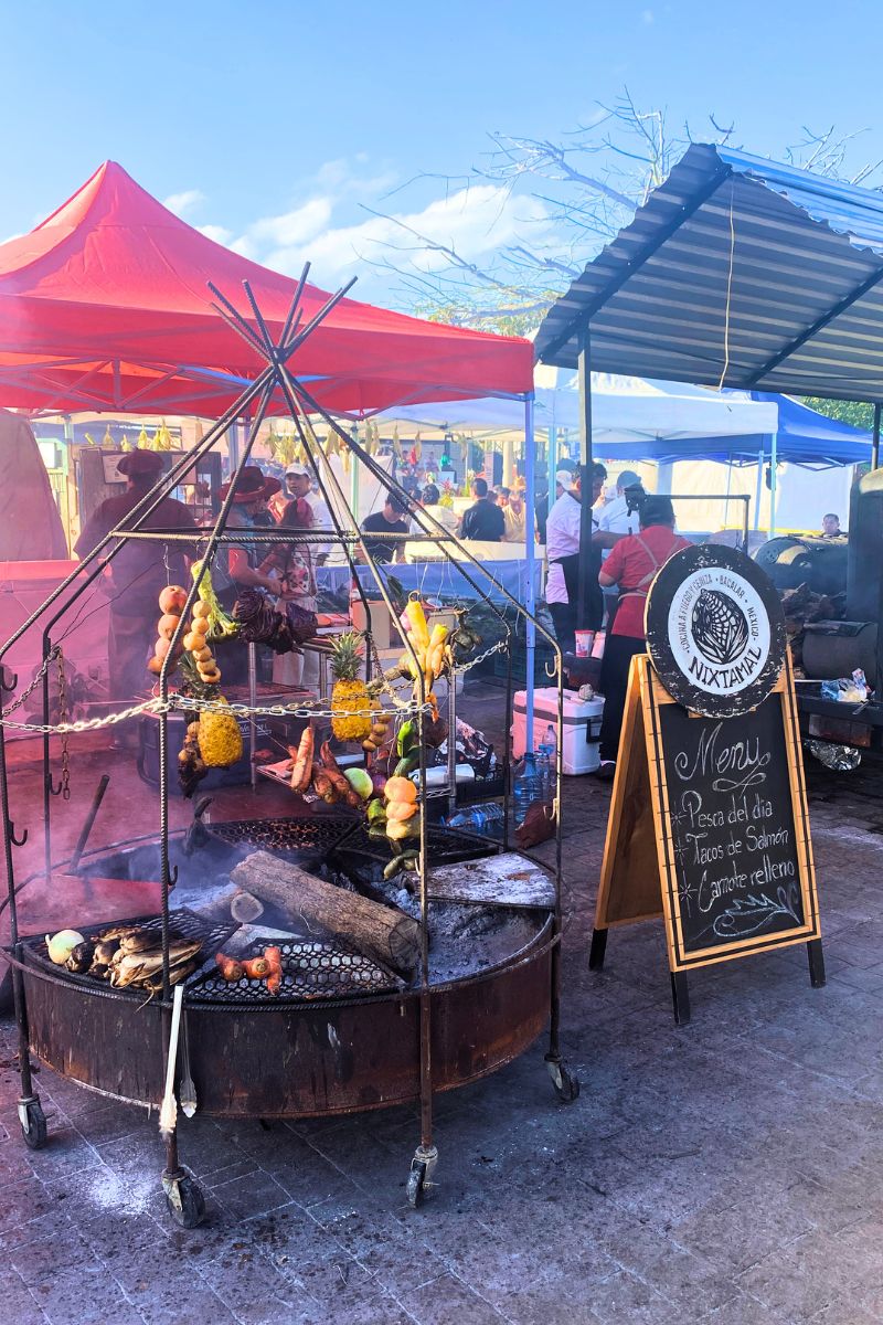 Meat and vegetables hung over a circular charcoal grill.