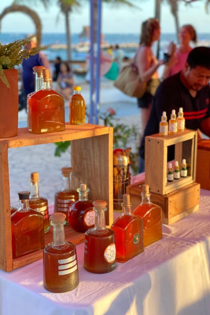 Honey in different shaped bottles being sold on a market stall.