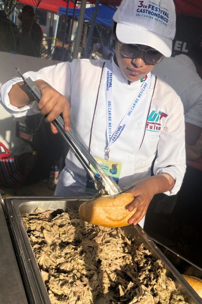 A lady putting shredded grilled meat into a torta.