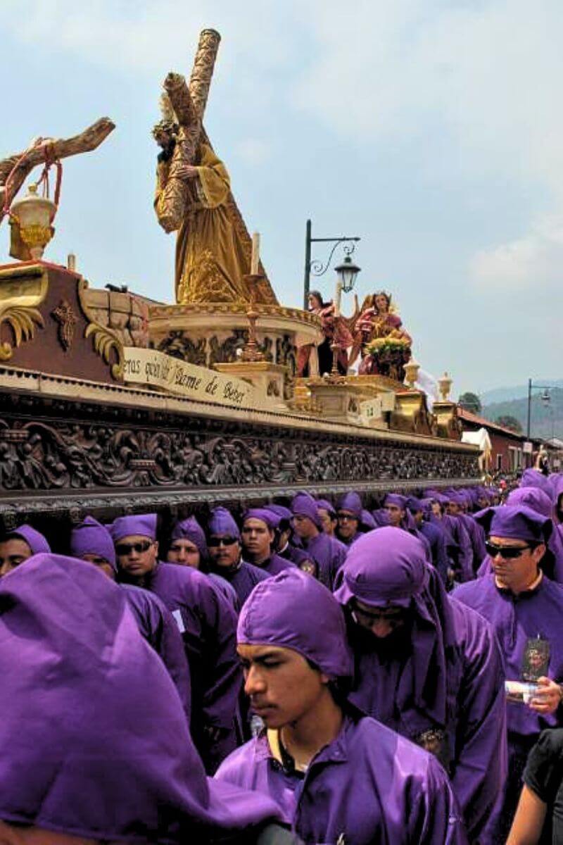 An enormous float with Jesus carrying his cross on it being paraded through town surrounded by men in purple robes.