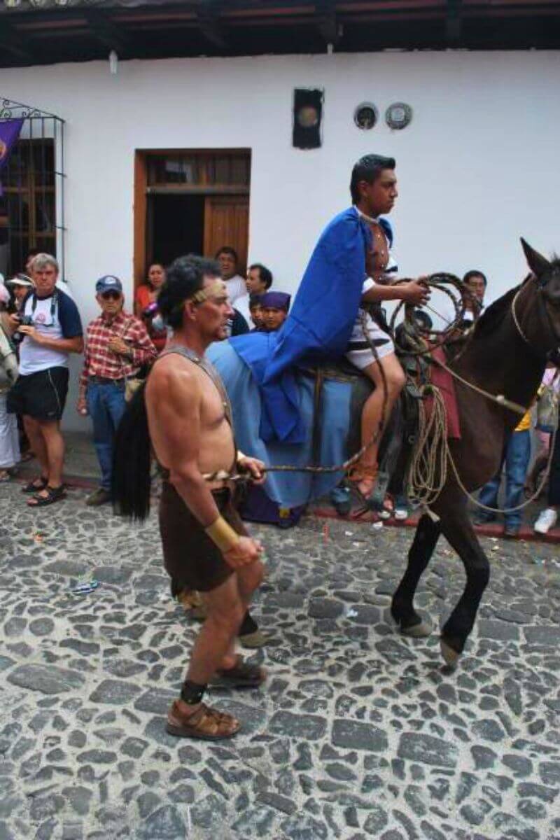 A man dressed as a roman on a horse, with another tied to the horse being taken to the crucifixion. Part of Via Crucis, the Way of the Cross.